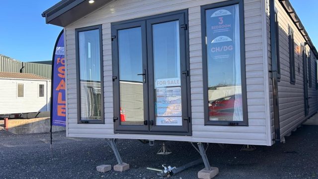 static caravan with patio doors lights on porch. sited on gravel