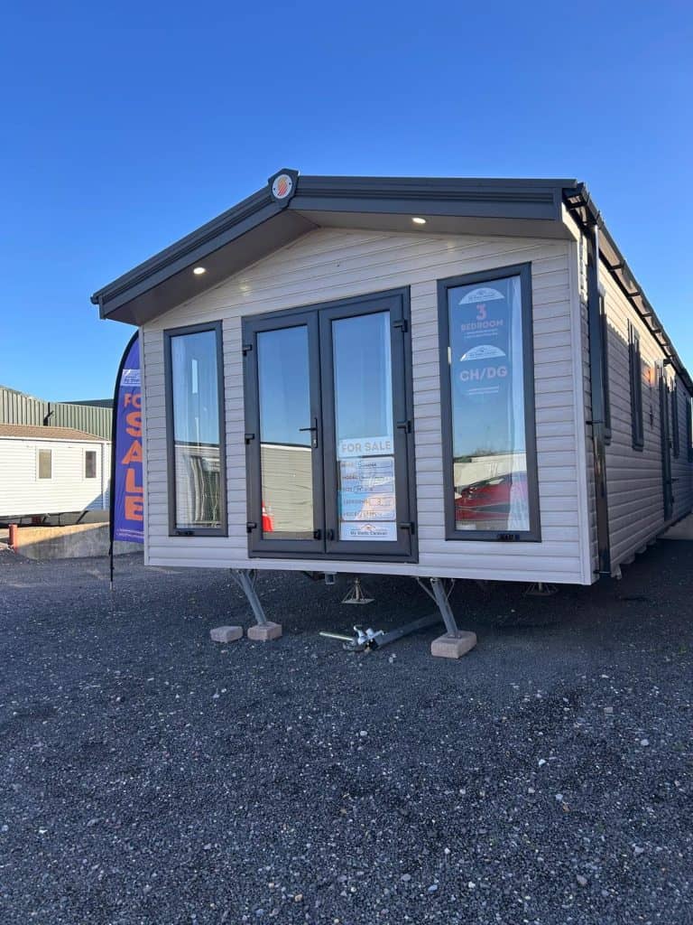 static caravan with patio doors lights on porch. sited on gravel