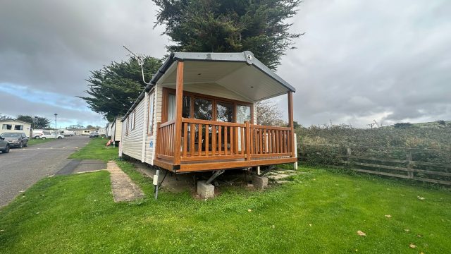 Static caravan with brown decking on grass pitch