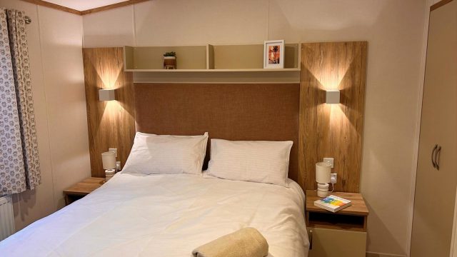 Double bed with bedside lamps on, bedside cabinets and above bed shelf