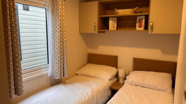 2 single beds in room with over bed shelving and storage