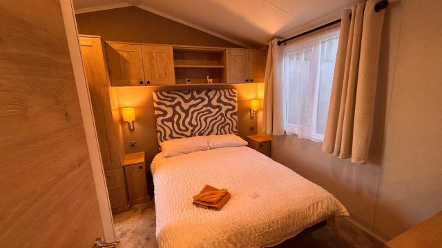 double bed with headboard, bed side wall lamps and over bed storage cupboards