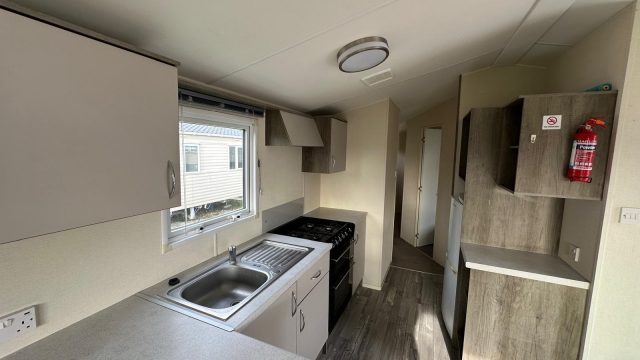 kitchen cupboards with sink by a window. Gas cooker and vinyl flooring