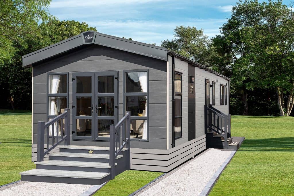 Glade with green lawn illuminated by sunlight. Wavy landscape in the background with tall trees.