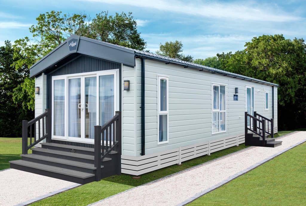 Glade with green lawn illuminated by sunlight. Wavy landscape in the background with tall trees.
