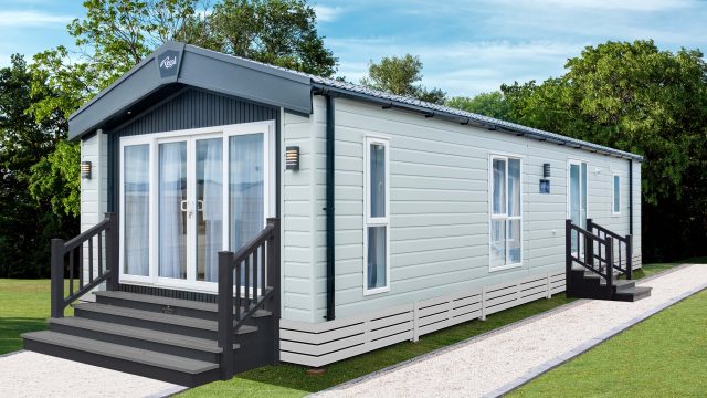 Glade with green lawn illuminated by sunlight. Wavy landscape in the background with tall trees.